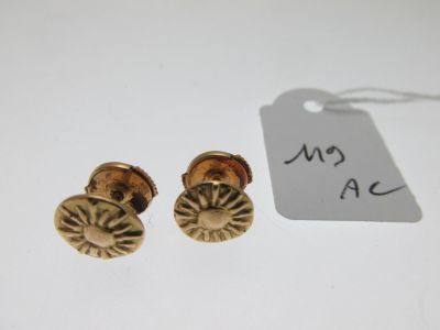 a pair of gold earrings with a tag on a white surface