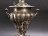 silver plated urn with two handles on a stand on a gray background