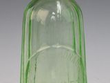 une bouteille en verre vert munie d'une poignée en laiton, posée sur une surface blanche