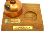 a small copper pot on a wooden base with a plaque