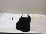 two white shirts and a black top are sitting on a white table