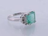 an emerald and diamond ring on a white surface
