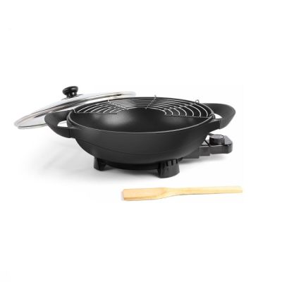 un wok noir avec une cuillère en bois sur fond blanc