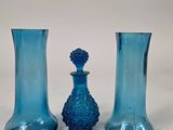 three blue glass vases sitting next to each other on a white surface