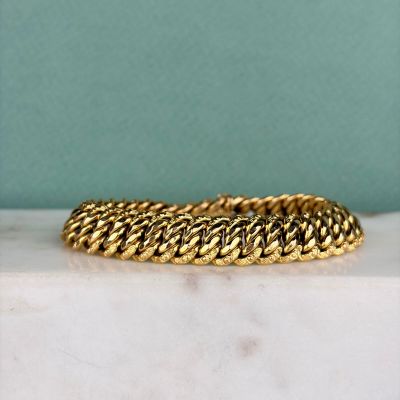 un gros plan d'un bracelet en or posé sur une surface en marbre