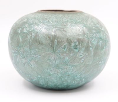 un vase vert posé sur une surface blanche, avec un fond blanc