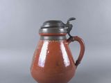 a red pitcher with a metal lid on a gray surface