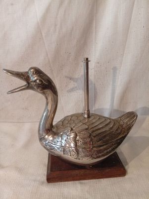 un canard en argent posé sur un socle en bois, avec un cure-dent dans le bec