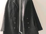 un manteau noir avec des bordures blanches, suspendu à un cintre accroché au mur