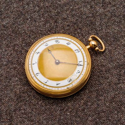 une montre de poche en or avec un cadran blanc sur un fond marron