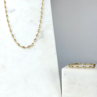Le collier et le bracelet en chaîne d'or sont exposés à côté d'un bloc de marbre blanc
