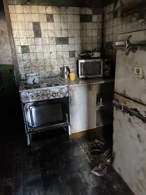 a dirty kitchen with a stove, microwave, and refrigerator