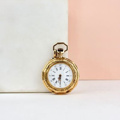 une petite montre de poche en or posée sur un bloc de marbre