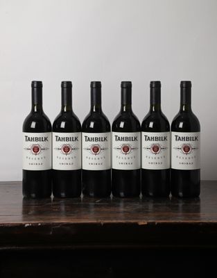 six bottles of red wine are lined up on a wooden table
