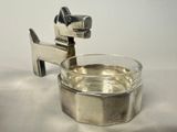 a silver dog shaped ashtray with a glass of water in it