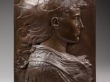 une plaque en bronze représentant une femme coiffée d'une coiffe