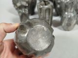 a person holding a metal object in front of a group of silver vases
