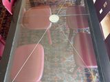 a glass table with four pink chairs and a rug