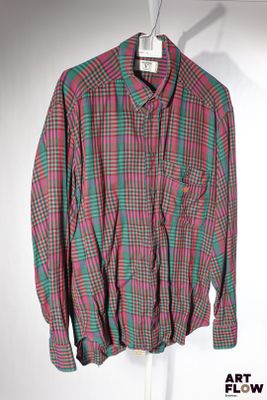 une chemise suspendue à un cintre sur un mur blanc, avec une chemise à carreaux rouges et verts