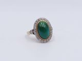 a close up of a ring with a green stone surrounded by diamonds