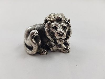 un gros plan d'une figurine de lion en argent posée sur une surface blanche
