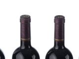 three bottles of red wine are lined up on a white surface