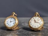 two small gold pocket watches sitting on a table