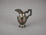 an old silver pitcher with a handle on a gray background