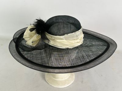 chapeau noir et blanc orné de plumes et d'un nœud, posé sur un porte-chapeaux
