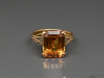 a close up of a ring with an orange stone on a reflective surface