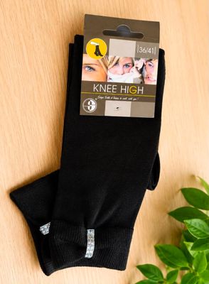 des chaussettes noires montant jusqu'aux genoux posées sur une surface en bois, avec une plante en arrière-plan