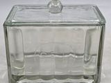 une boîte en verre avec un couvercle en verre, posée sur une surface blanche