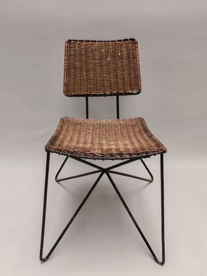 une chaise en osier marron avec des pieds en métal noir et une assise en osier