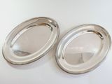 two oval silver trays on a white table with a white background