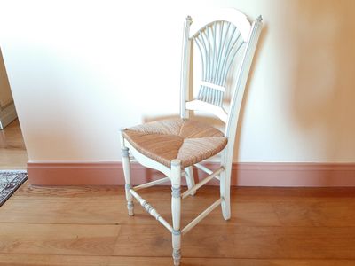 une chaise blanche avec une assise en osier, dans un coin de la pièce