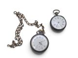 two pocket watches sitting on a chain on a white surface