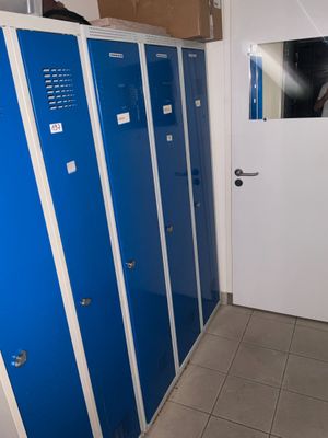 Plusieurs casiers bleus sont alignés dans une pièce dont la porte est blanche.