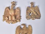 trois broches en forme d'aigle doré sur un fond blanc, avec un œuf doré