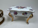 a small white box with flowers on it next to a small gold box