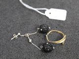 une paire de boucles d'oreilles noires et dorées et une bague dorée posées sur une surface grise