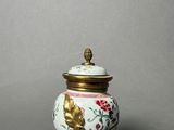 a small white vase with a gold lid on a gray surface