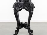 une table noire richement décorée, avec un plateau en marbre, posée sur un sol gris