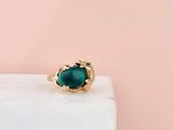 a gold ring with a green stone on top of a marble block