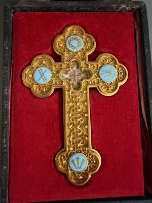 une croix en or richement décorée, sertie de pierres bleues, dans un coffret rouge
