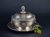 an antique silver plate with a lid and a flower on a black background