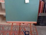 a green chalkboard on a wooden easel in front of a bookshelf