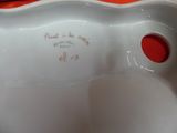 a white porcelain bowl with a red handle on a table