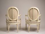 two white chairs with a striped upholstered back and arms