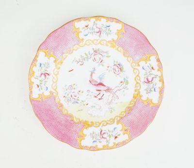 une assiette rose et jaune ornée d'un oiseau, posée sur un fond blanc