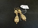 une paire de boucles d'oreilles en or ornées de perles, posées sur un fond noir